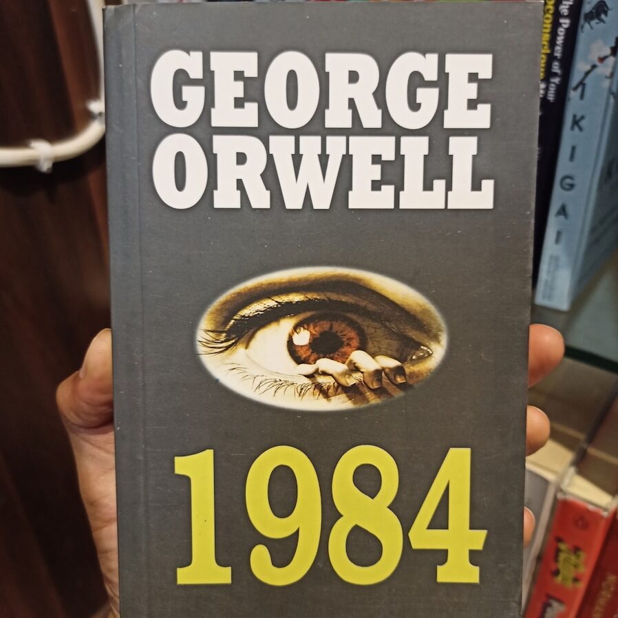 a person holding up a book in front of a book shelf